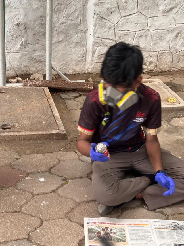 Adithya in a respirator and gloves spray-painting the car on the ground